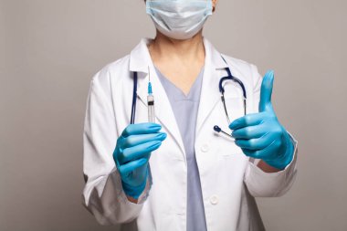 Doktorlar enjeksiyonlu eller, doktor şırıngayı tutuyor ve baş parmağını gösteriyor.