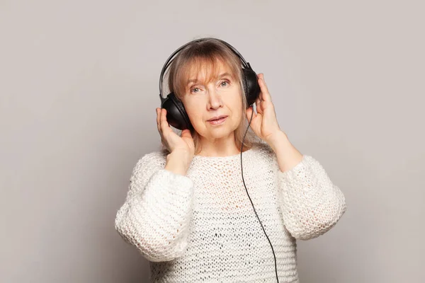 熟女は 白いスタジオの壁の背景にヘッドフォンで音楽を聞いてリラックス — ストック写真