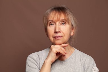 Kahverengi arka planda kameraya bakan sevimli yaşlı bayan.