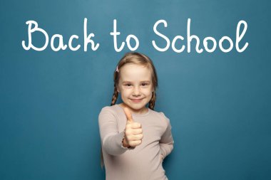 Sevimli liseli kız mavi arka planda baş parmağını gösteriyor ve gülümsüyor. Okul konseptine dönelim.