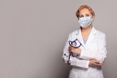 Sağlık maskesi takan doktor gri arka planda duruyor.