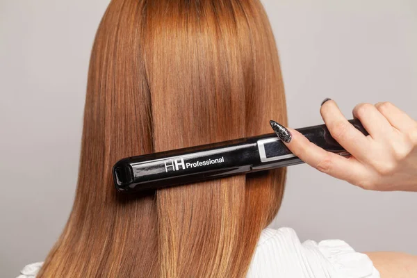 Hair straightening. Straightener and healthy female hairstyle