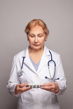 Doktor elinde beyaz haplı gümüş broşürler tutuyor.