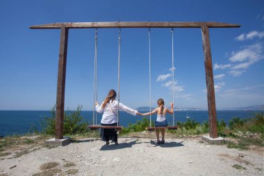 Mutlu anne ve kız yaz mevsiminde birlikte salıncak oynuyorlar, mutlu aile kavramı.