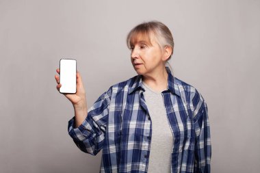 Olgun kadın reklam ve ürün yerleştirme için boş ekranlı akıllı telefon tutuyor.