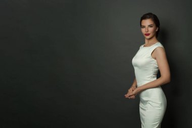 Siyah pankartta poz veren beyaz ipeksi elbiseli neşeli ve çekici genç bir kadın.