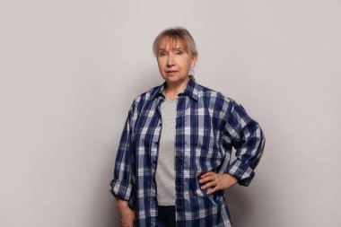 Dostça gülümseyen orta yaşlı kadın gri arka planda duruyor.