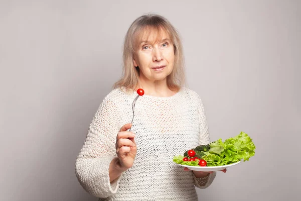可愛いです魅力的な陽気な中年シニア女性保持で彼の手トマトミックス野菜上の灰色のバナー背景 — ストック写真