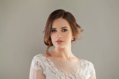 Gri stüdyo arka planında kameraya bakan zarif, zarif, esmer bir kadın.