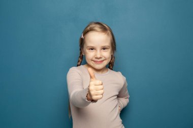 Cute happy smiling kid girl showing thumb up on blue background
