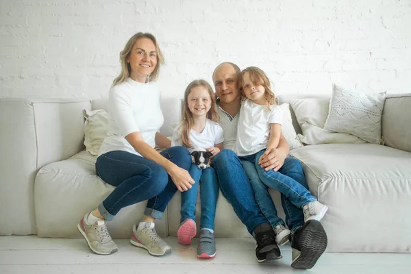Family and relationship concept. Beautiful and happy smiling young family in white T-shirts are hugging and have a fun time together while sitting on sofa and looking on camera