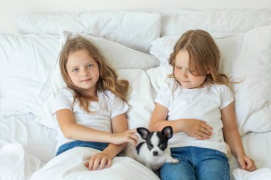 Happy kids girls sisters with puppy dog pet lying on the bed