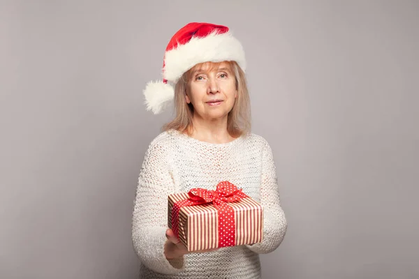 Studio portrait of happy beautiful middle age woman ready to celebrate Christmas and New Year, posing and holding Xmas gift box present