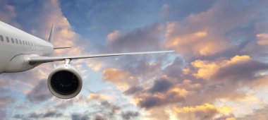 Bulutların üzerinde dramatik günbatımı ışığında uçan ticari beyaz uçak. Seyahat ve ulaşım kavramı