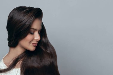 Çekici, sevimli bir kadın model yüzü. Yakından. Gri pankartta uzun siyah saçlı ve makyajlı mükemmel bir genç kadın.