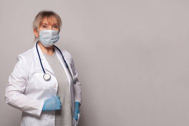 Doctor in medical mask, professional uniform coat, blue gloves and stethoscope standing on grey banner background. Healthcare and medicine concept