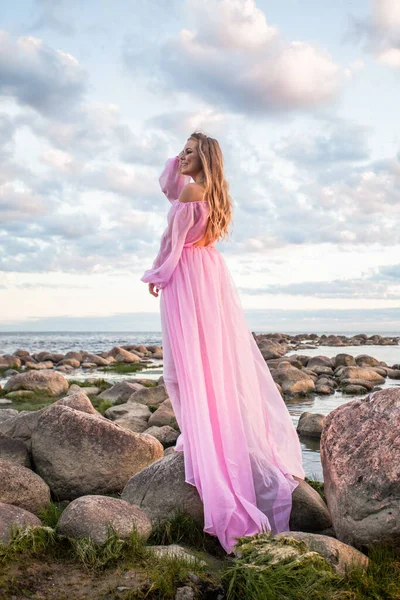 Young female model in pink dress against summer sunset sky and clouds background