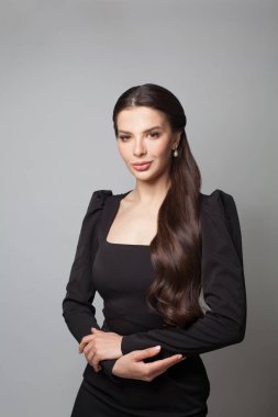 Gri arka planda duran siyah elbiseli güzel kadın.