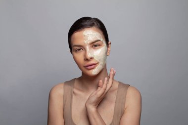 Gri arka planda kozmetik kil maskeli spa modeli kadın