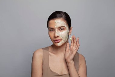 Cilt bakımı. Gri arka plana maske takan çekici bir kadın spa modeli.