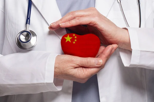 Chinese doctor holding heart with flag of China background. Healthcare, charity, insurance and medicine concept