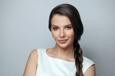 Gri arkaplanda gülümseyen uzun siyah saçlı ve makyajlı güzel esmer model kadın.