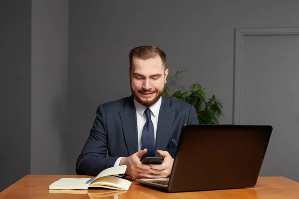 Lächelnder Geschäftsmann Sitzt Seinem Büro Und Benutzt Laptop Und Smartphone — Stockfoto