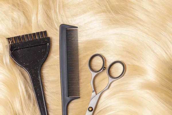 Professional hairdresser tools, scissors and comb on golden blonde hair background.