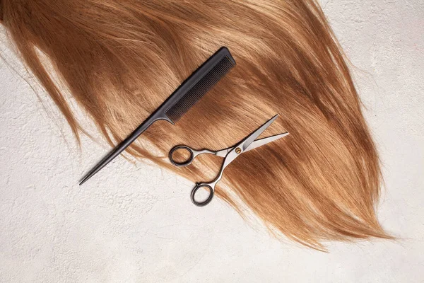 Long healthy ginger hair, professional scissors and comb on white background