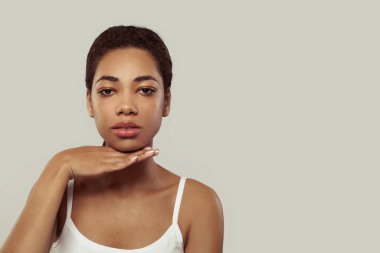 Beyaz arka planda çenesine dokunan parlak tenli çekici genç bir manken.