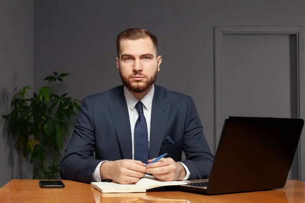 Thoughtful focused clever businessman holding pen with hands wearing suit working on deadline project using laptop indoor