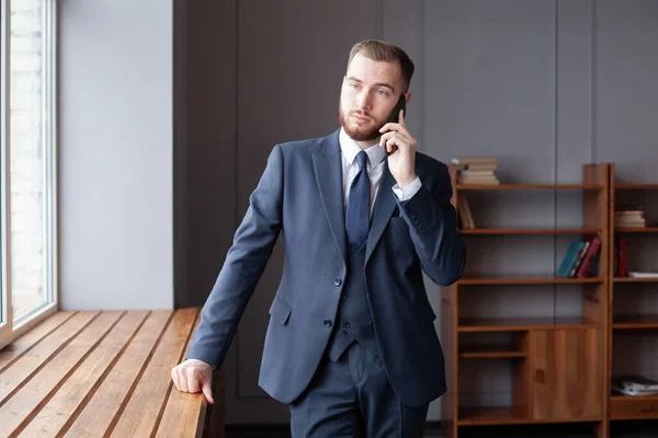 Young man in blue suit talking on smart phone in the office