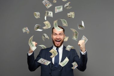 Gri arka planda yığınla parası olan mutlu iş adamının portresi.