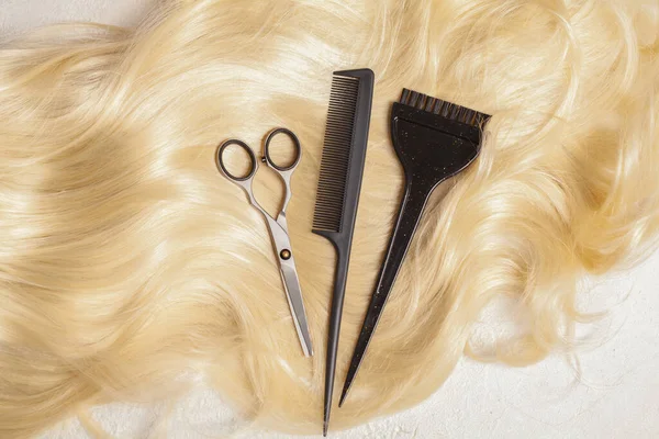 Hairdresser\'s scissors with comb on strand of blonde hair background, top view