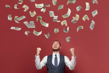 Güçlü neşeli iş adamı kırmızı arka planda para yağmurunda duruyor.