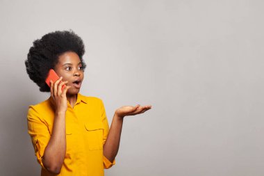 Beyaz duvar arkasında akıllı telefonu olan mutlu, şaşkın bir kadın.