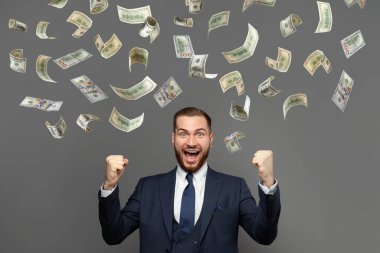 Heyecanlı, mutlu, başarılı adam para altında duruyor, gri arka planda yağmur yağıyor.