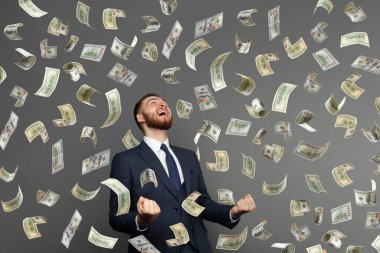 Yüzlerce dolarlık banknotlar havada uçuşurken iş adamı başarısı için seviniyor.