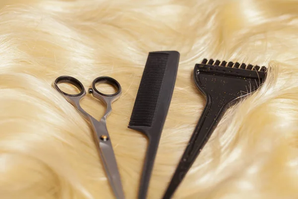 Professional scissors, comb and hairdressing brush on blonde hair
