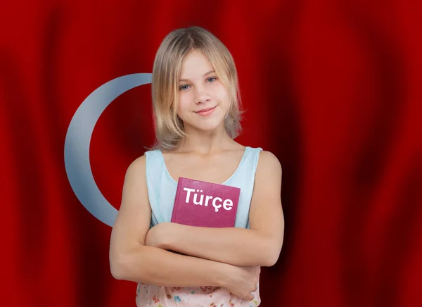 Young smiling girl and textbook with inscription turkish in turkish language on flag of Turkey background
