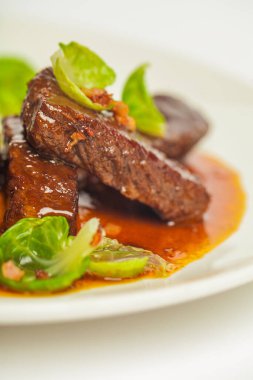 Kırmızı soslu leziz dana yanakları ve yeşil. Beyaz arkaplanda beyaz bir plakaya yaklaş