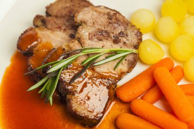 Beyaz tabakta sebzeli lezzetli domuz eti.