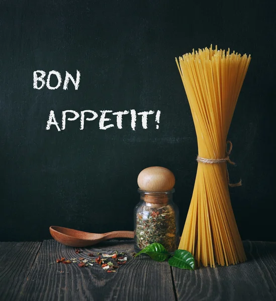 Spaghetti and spices on blackboard background. bon appetit text — Stock Photo, Image