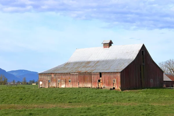Full profile view of an old farm building including windows and doors with a metal roof and agricultural land in a mountain valley.