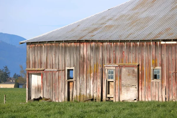 Partial profile view of an old farm building siding including windows and doors with a metal roof.