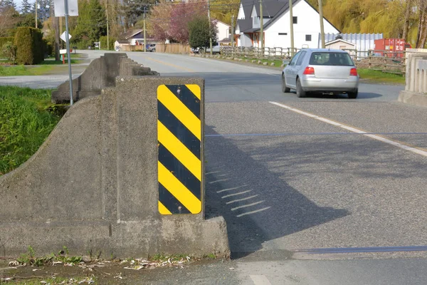 A rectangular black and yellow reflective safety sign is mounted on a small bridge crossing to draw attention to the cement structure.