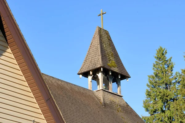 Medium view of a simple church steeple with a Christian cross on top representing the faith.