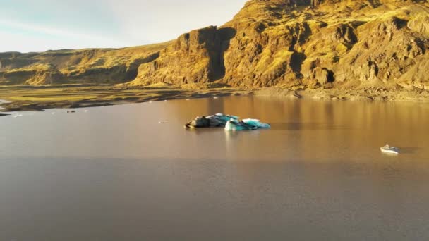 Drone sulla laguna con ghiaccio blu verso il paesaggio roccioso illuminato dal sole — Video Stock