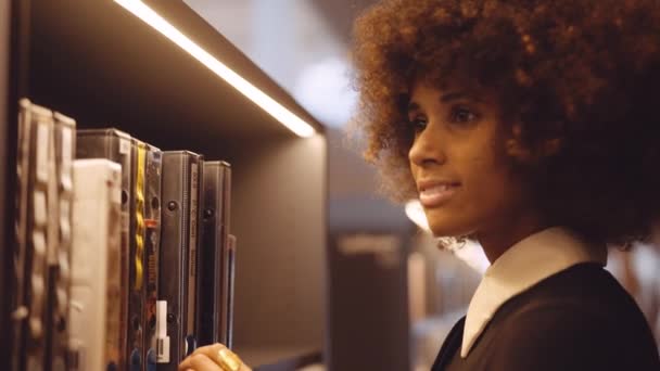 Mujer joven que elige el libro de estante de la biblioteca — Vídeo de stock