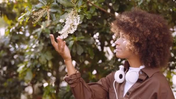 Усміхнена молода жінка торкається квітів у ботанічному саду — стокове відео